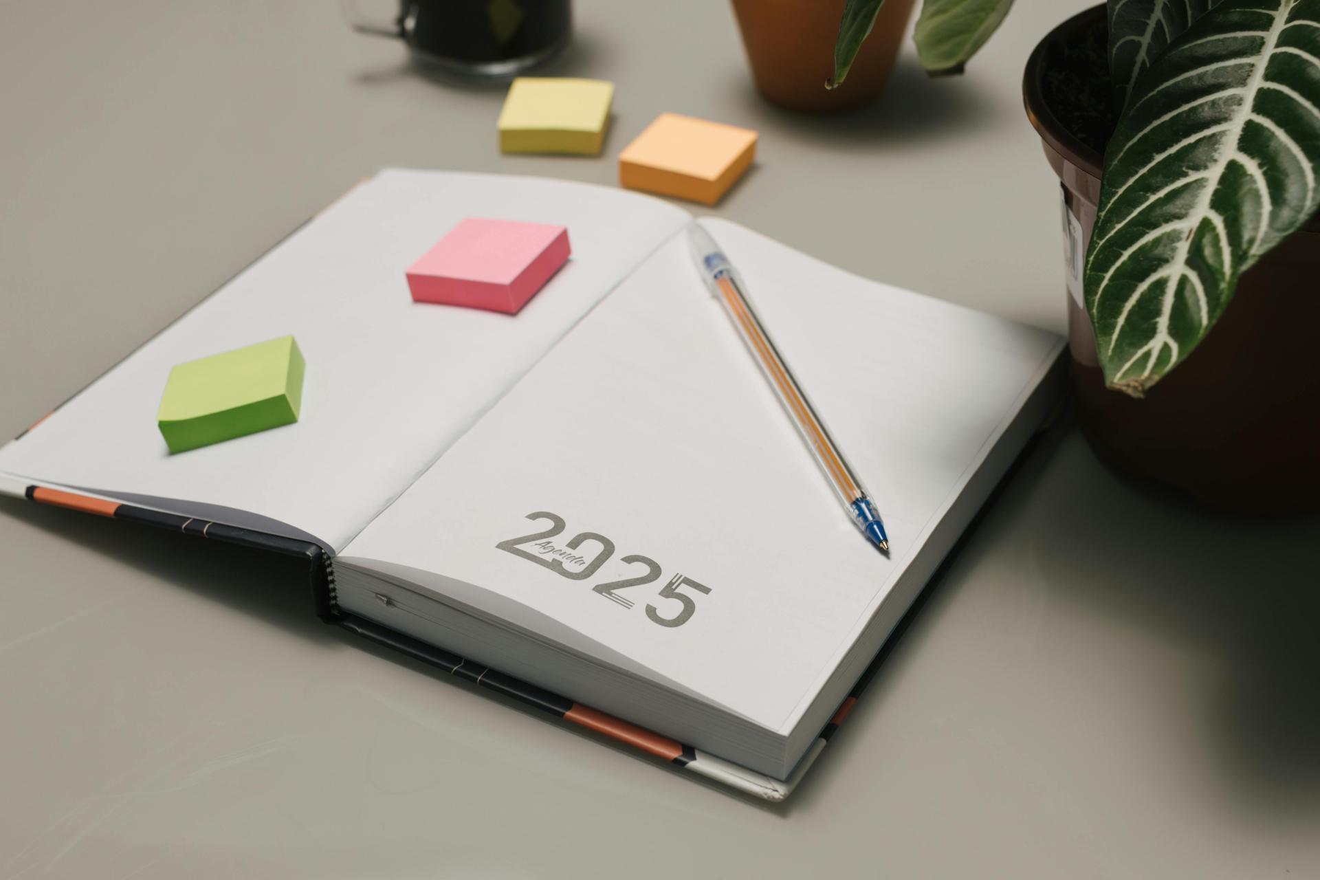 Otwarty kalendarz na 2025 rok, leżący na biurku wraz z długopisem i karteczkami samoprzylepnymi